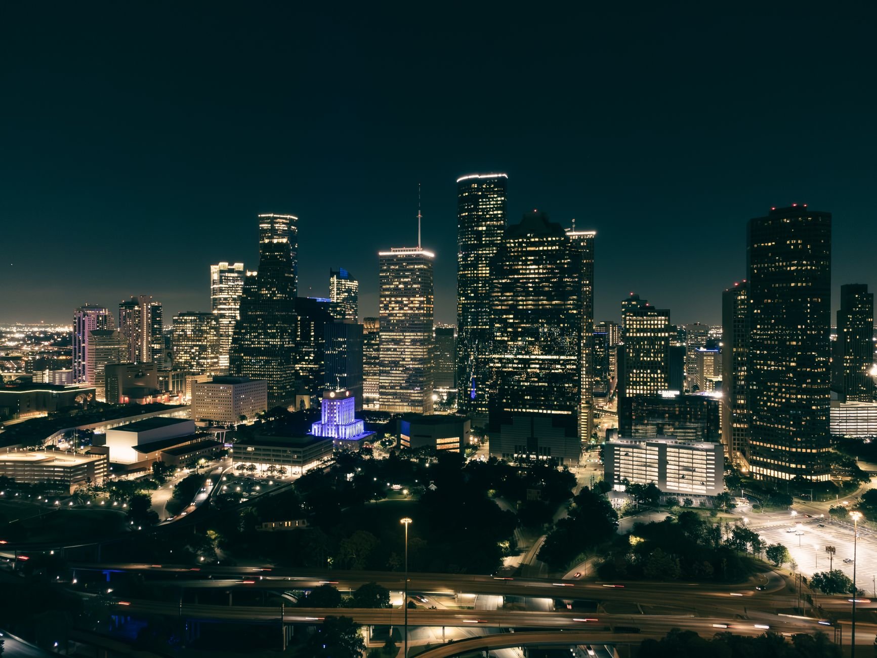 Aerial view of a vibrant city skyline at night with illuminated skyscrapers and roads.